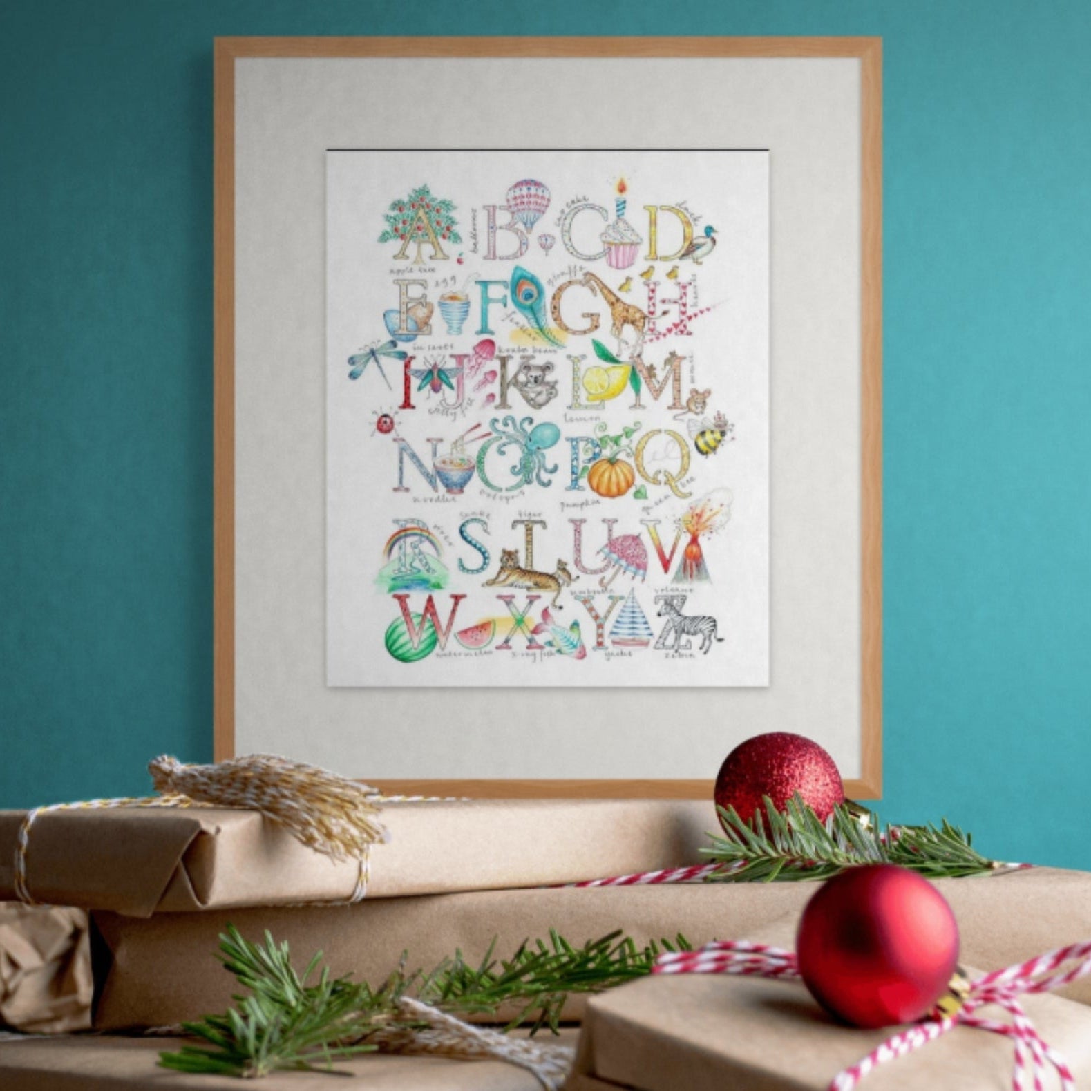 Framed alphabet print with Christmas decorations on a teal wall